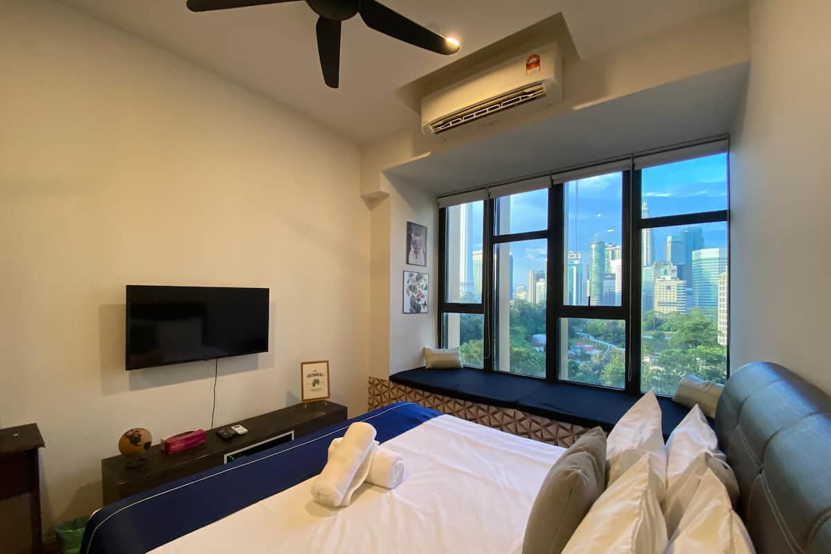 Une chambre d’hôtel équipée d’un lit, d’une télévision, d’une fenêtre donnant sur la ville et d’un appareil de climatisation.