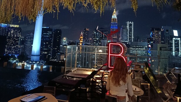 Un bar en la azotea con vistas al horizonte de una ciudad, incluyendo un edificio alto con un campanario.