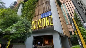 Un edificio moderno con un llamativo letrero de 'CEZONZ', rodeado de vegetación y otros edificios altos.