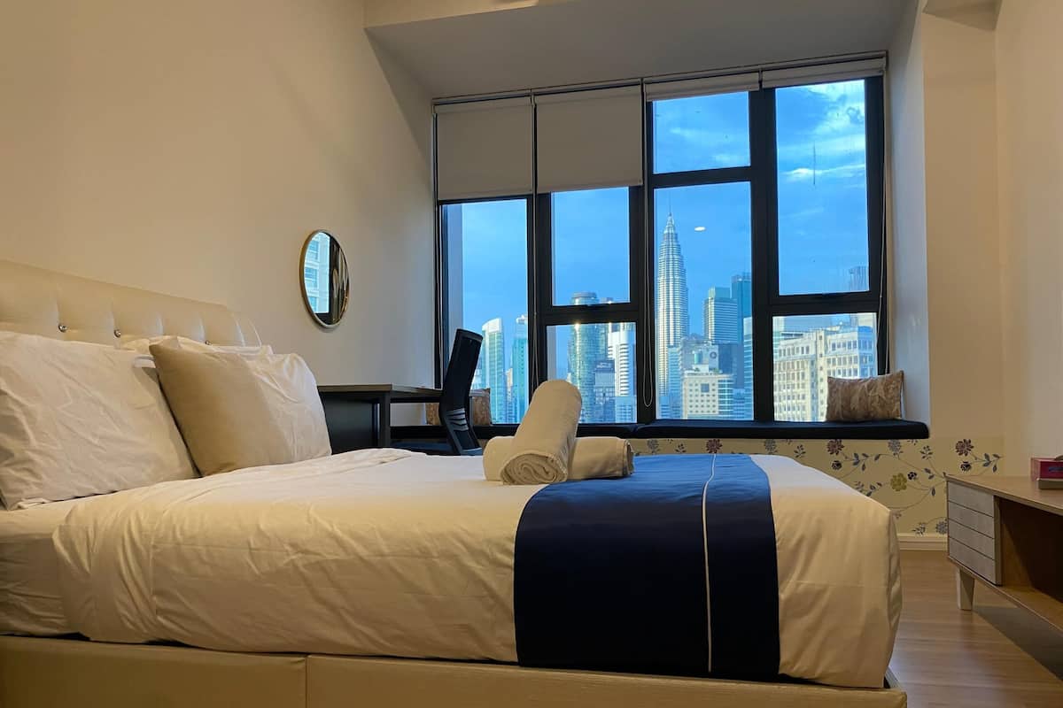 Une chambre d’hôtel avec un grand lit, un bureau et une vue sur les toits de la ville, grâce à de grandes fenêtres.
