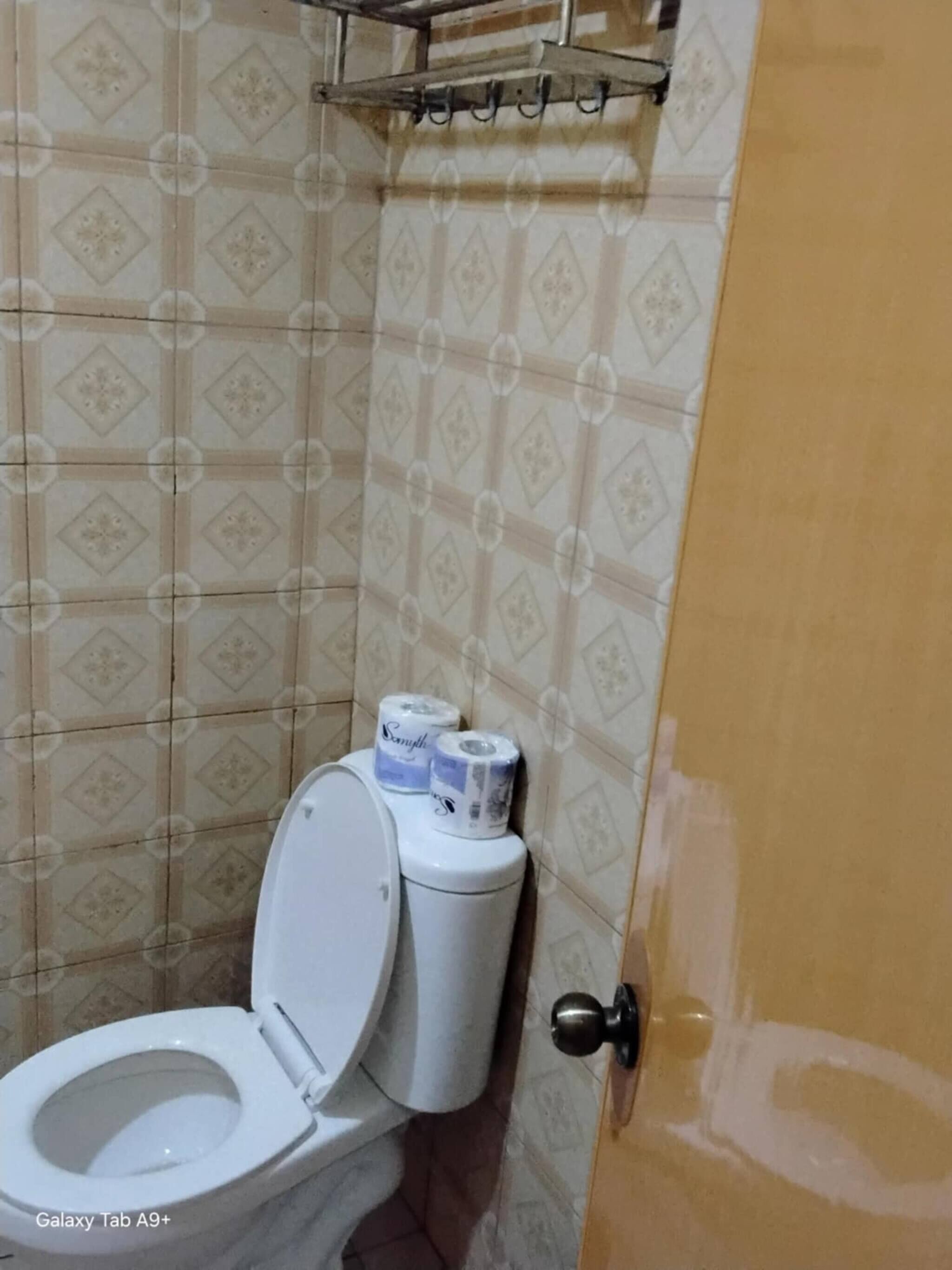 Un baño con inodoro, azulejos estampados y una puerta con una reparación visible.