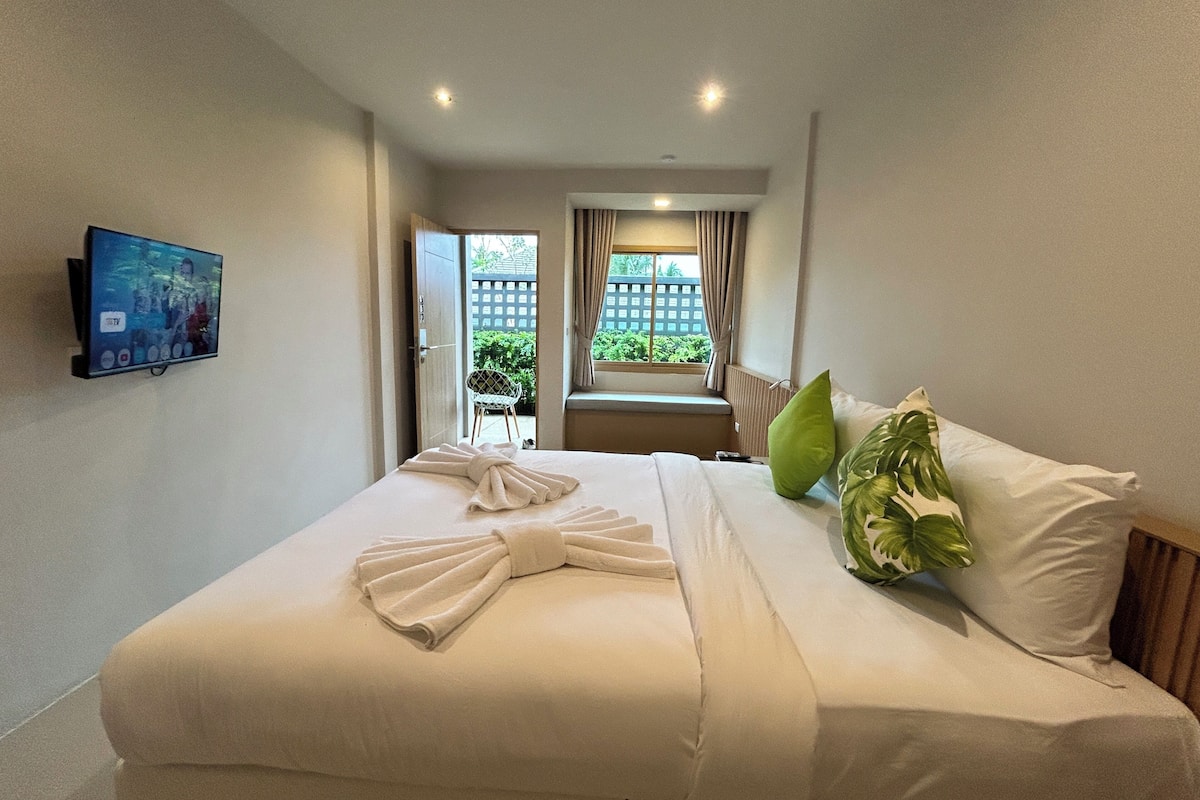 A hotel room with a bed, a TV mounted on the wall, and a view of the outside through a window.