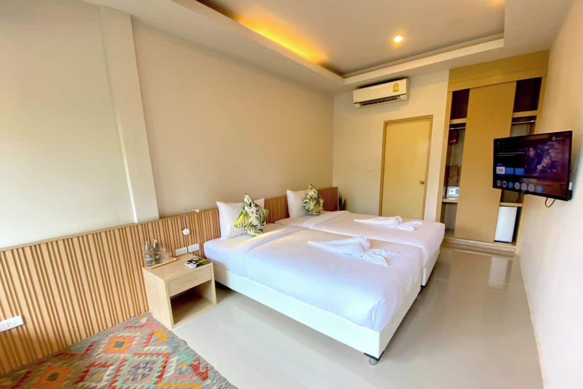 A hotel room with two beds, a TV, an air conditioning unit, a bedside table, and a patterned rug.
