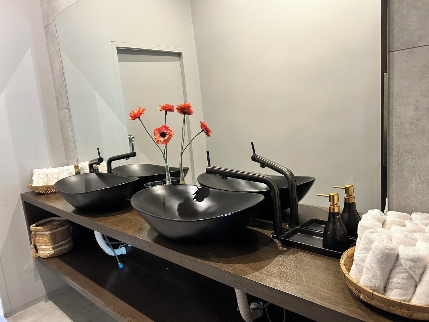 Un baño moderno con dos lavamanos tipo lavabo negros, un espejo y un perchero con toallas blancas.