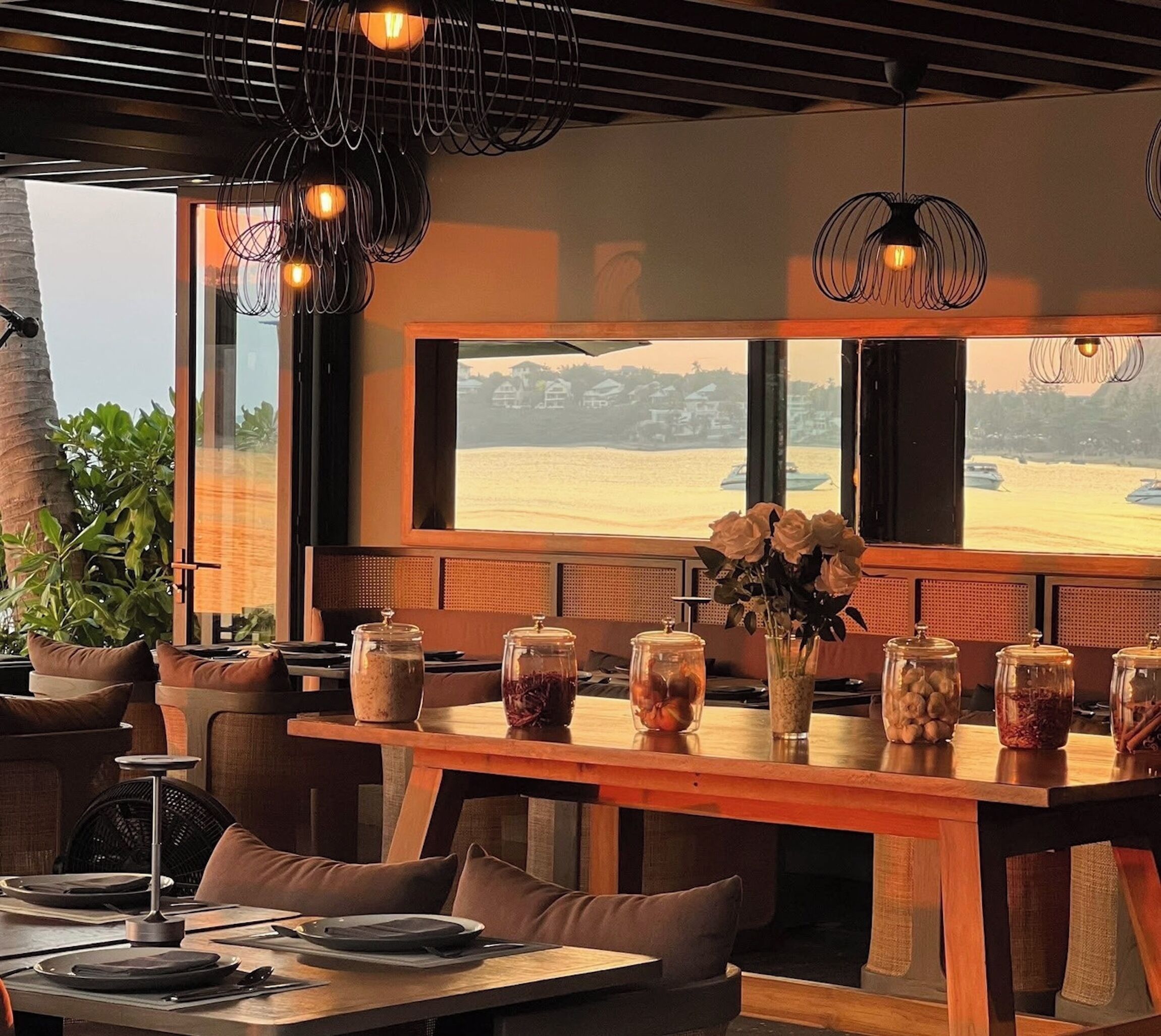 A restaurant with a large window view of a beach, wooden tables, and chairs.