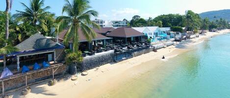 A beachfront hotel with outdoor seating, palm trees, and a clear view of the ocean.