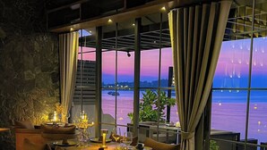 A restaurant with a view of the water, tables set with wine glasses and plates, and a stone wall. - Transit Samui Resort (Koh Samui)