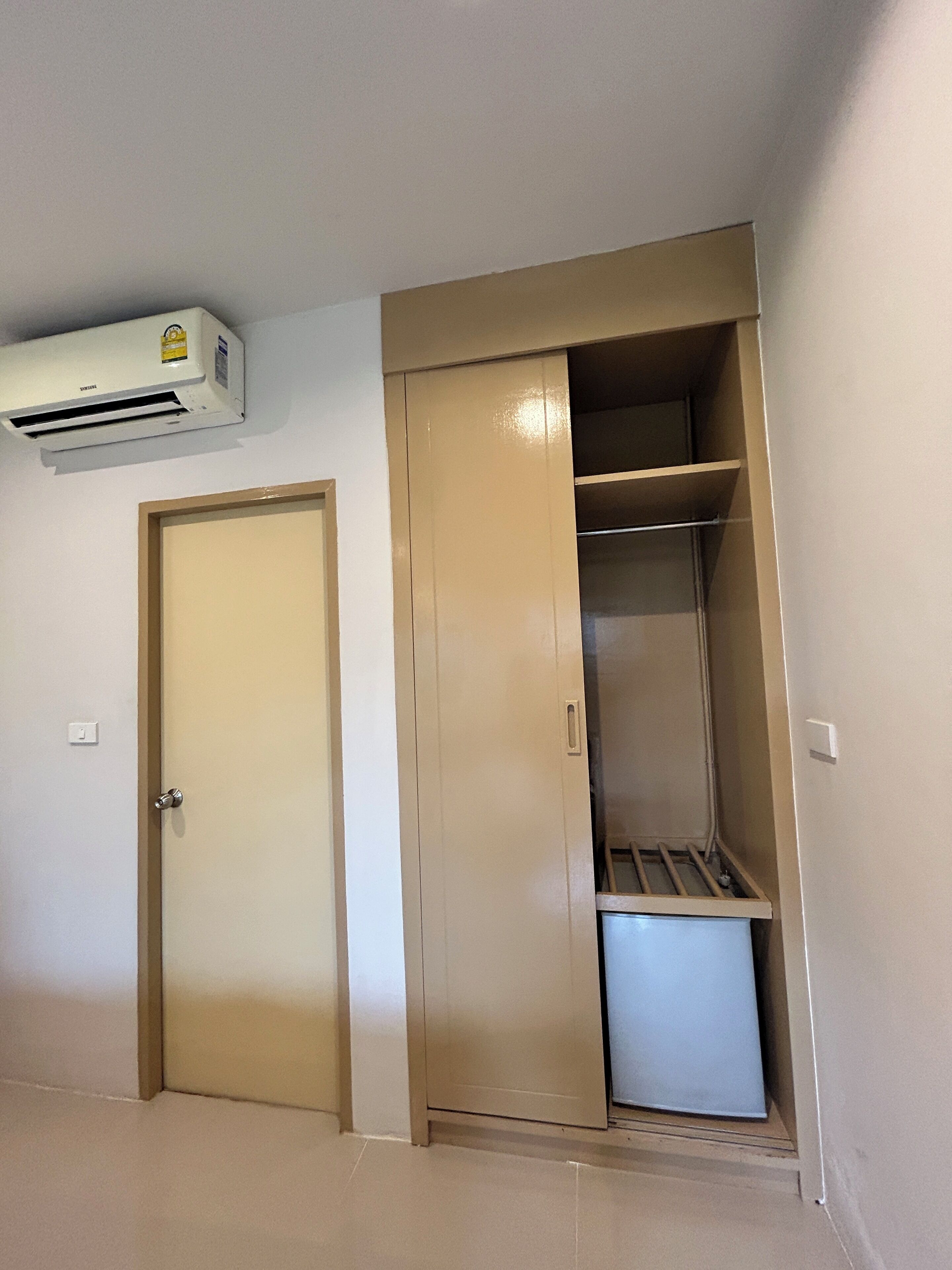 Een kamer met een beigekleurige deur, een kast met planken en een airconditioning die aan de muur is bevestigd.