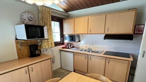 A compact kitchen with wooden cabinets, a microwave, a sink, and a dining table.