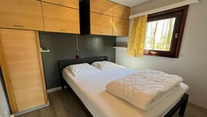 A bedroom with a bed, wooden wardrobe, and a window with curtains.