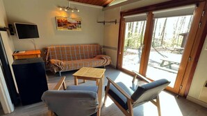 A cozy room with a plaid sofa, two chairs, a small table, a TV, and a large sliding glass door leading to an outdoor area.