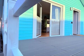 Ein blaues Haus mit Veranda und Glasschiebsetüren, die in einen Innenbereich mit Pflanze und Küchenzeile führen.