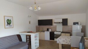 Un espacio habitable compacto con kitchenette, un sofá, una pequeña mesa de comedor y un televisor.