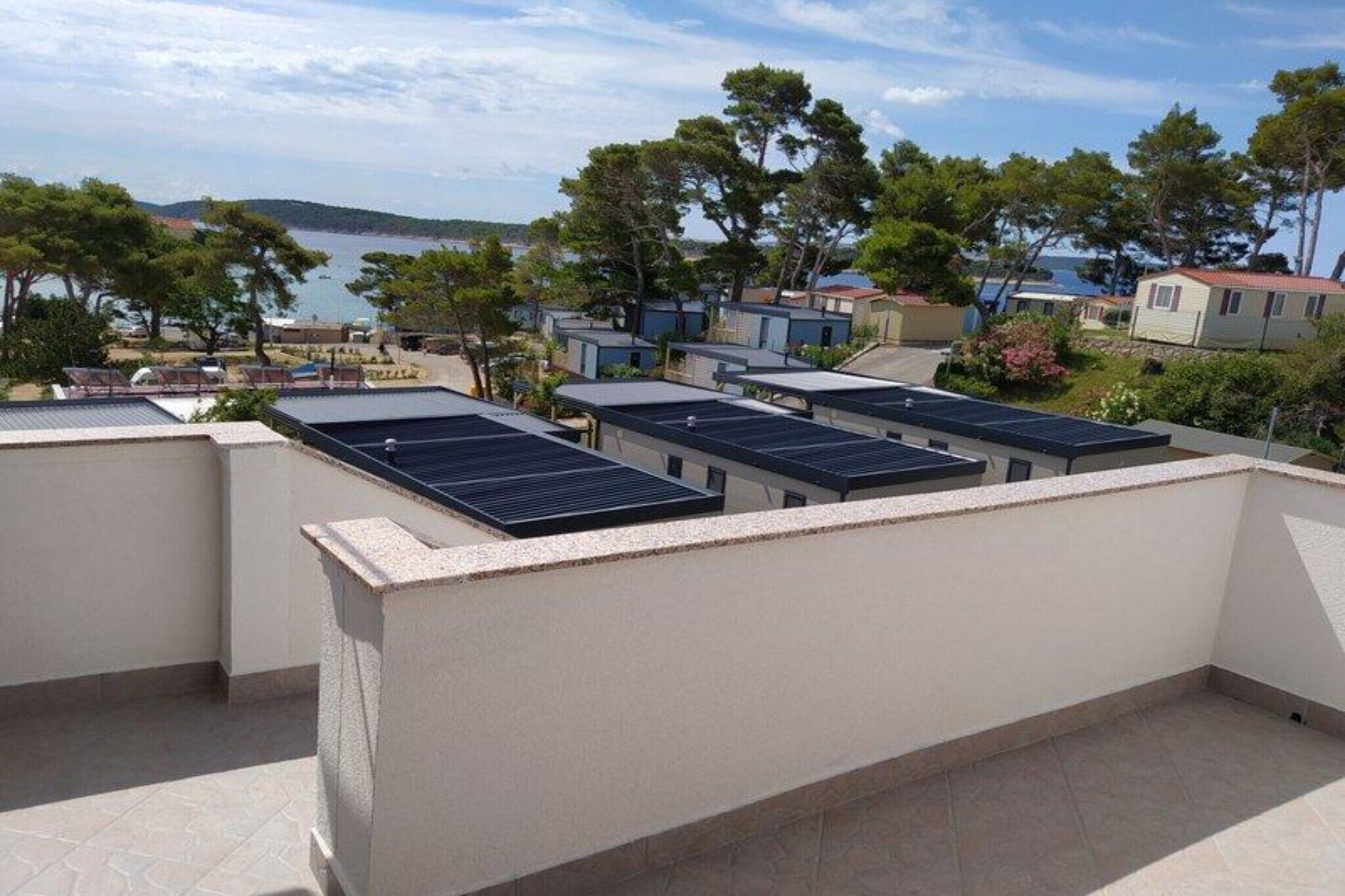 A rooftop with solar panels, a view of the sea, and a row of houses in the background.