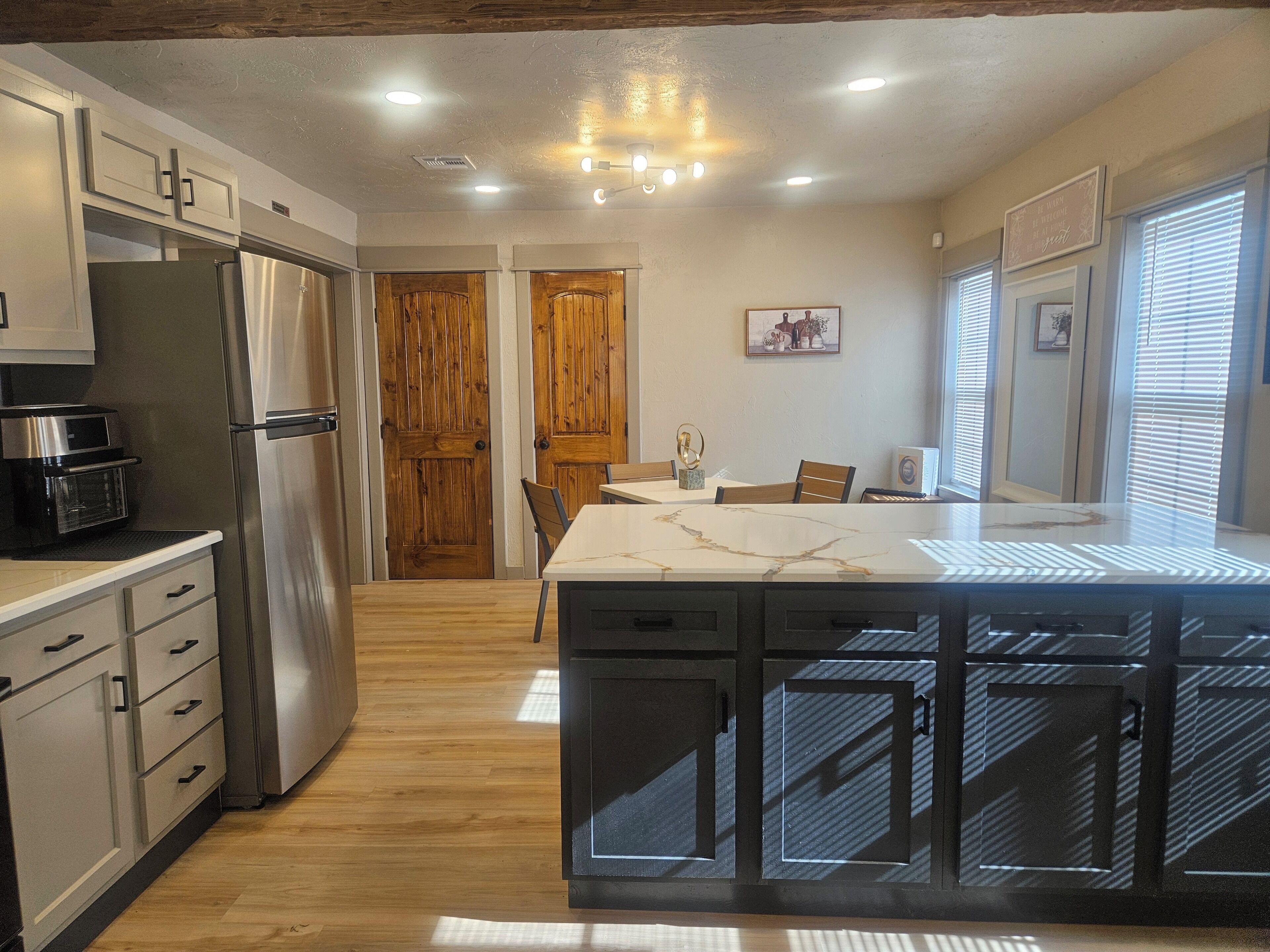 A modern kitchen with wooden cabinets, a stainless steel refrigerator, a built-in oven, and a marble island with a sink.