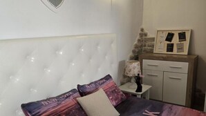 A neatly arranged bedroom with a tufted headboard, a bed with pillows featuring 'New York' prints, a bedside table with a lamp, and a small cabinet with a framed picture. - Studio apartment Angir Martina (Brodarica)