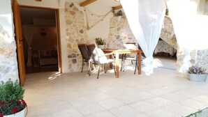 A stone-walled patio with a table and chairs, a potted plant, and a doorway leading to an interior space. - Studio apartment Angir Martina (Brodarica)