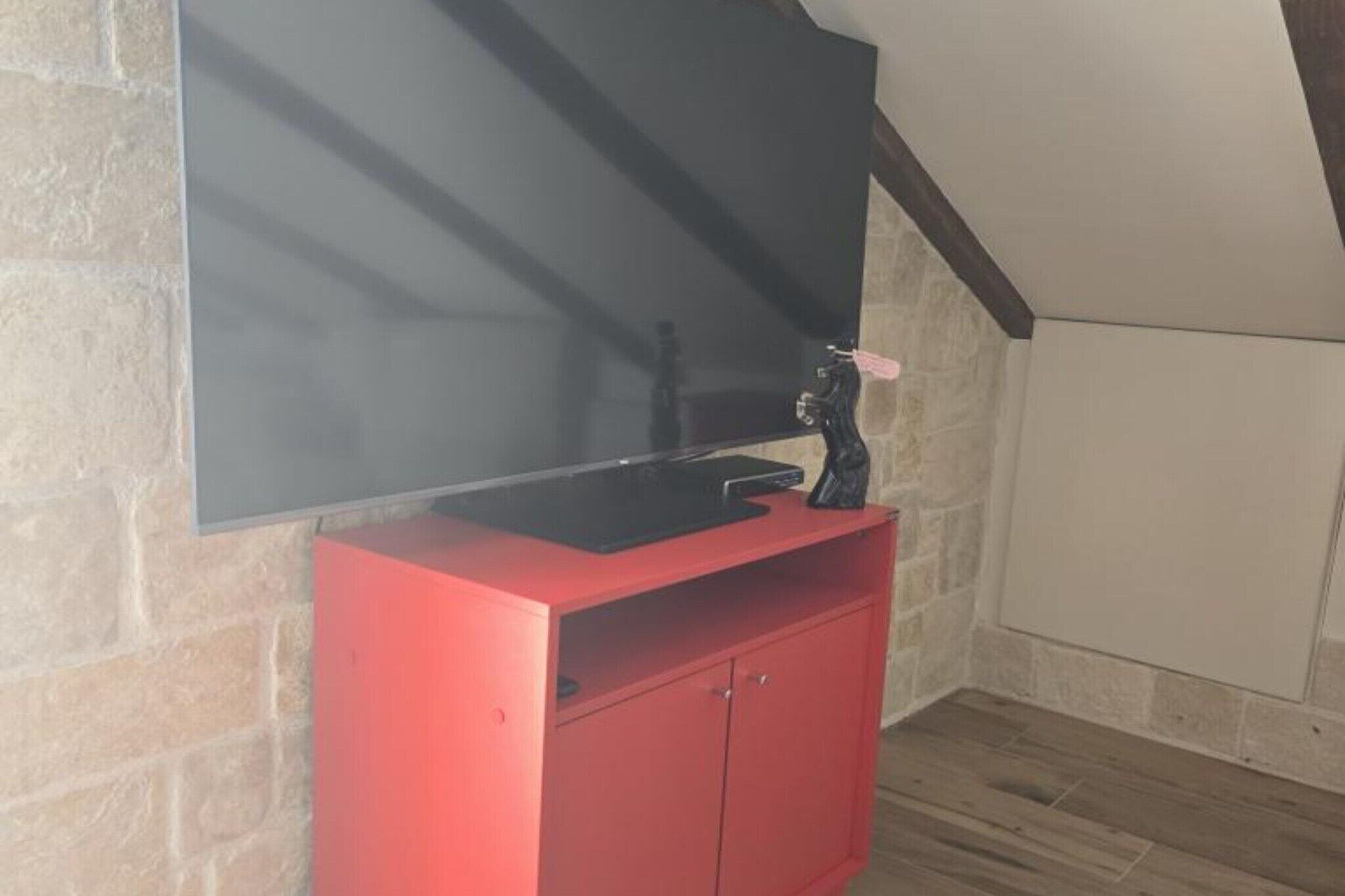 Eine rote Unterhaltungsecke mit Flachbildfernseher, einer kleinen Vitrine und einem dekorativen Gegenstand darauf.