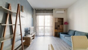 Un salon avec un canapé bleu, des étagères en bois, un bureau et une lampe.