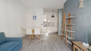 Un salon moderne comprenant un canapé, une table à manger et des chaises, un coin cuisine et un mur d’accent gris agrémenté d’étagères.