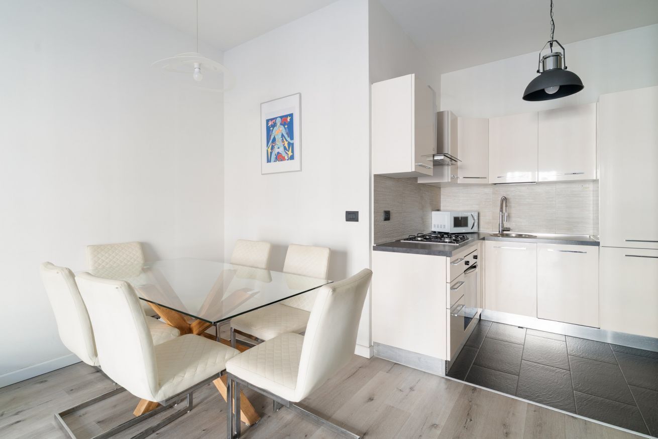 Een moderne keuken met witte kasten, een glazen eettafel en een hanglamp.