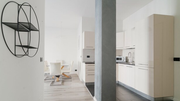 Une cuisine moderne avec des meubles blancs, une colonne grise et une œuvre d’art abstraite noire accrochée au mur.