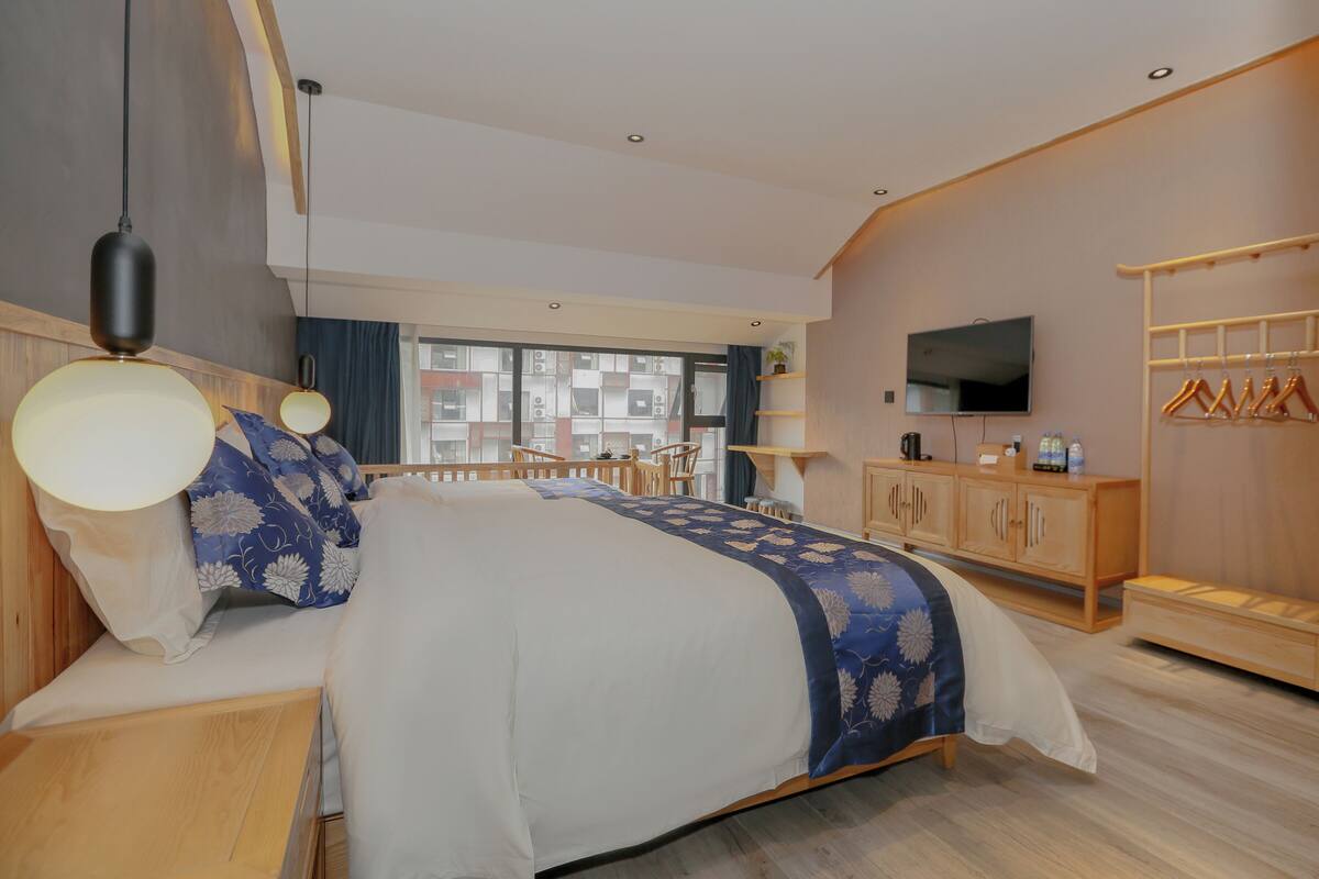 A modern hotel room with a large bed, a TV, a wardrobe, and a balcony with a view of the city.