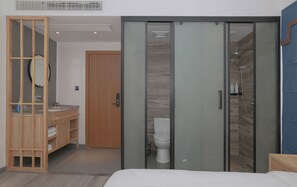 Un dormitorio con cama, armario de madera, baño con inodoro y ducha, y espejo.