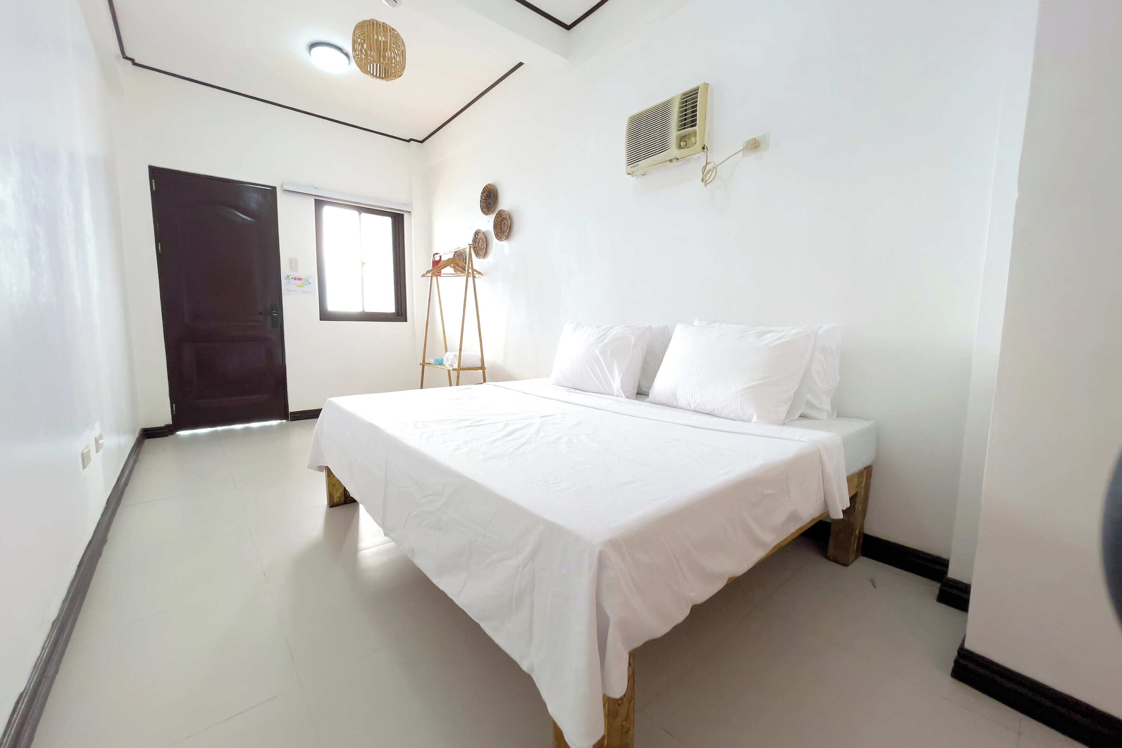 Un dormitorio con cama, ventana, puerta y aire acondicionado instalado en la pared.