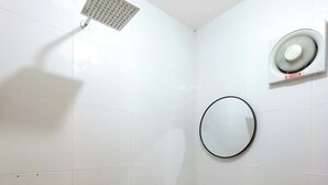 A bathroom with white tiled walls, a ceiling-mounted showerhead, a wall-mounted circular mirror, and a visible toilet. - Salacia Beachfront Resort (Bauan)