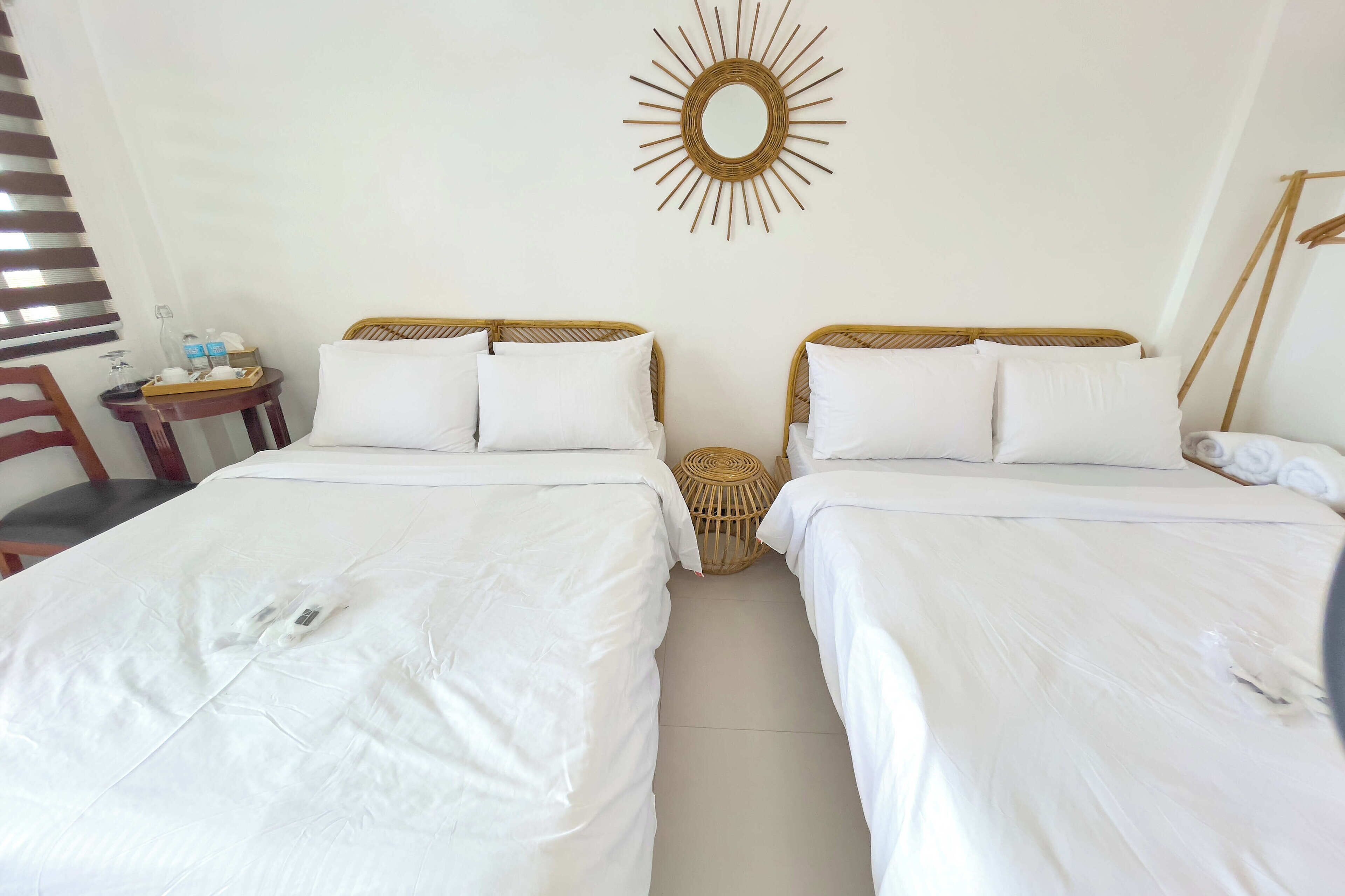 A hotel room with two single beds, a small table with toiletries, a wicker side table, and a wall-mounted mirror.