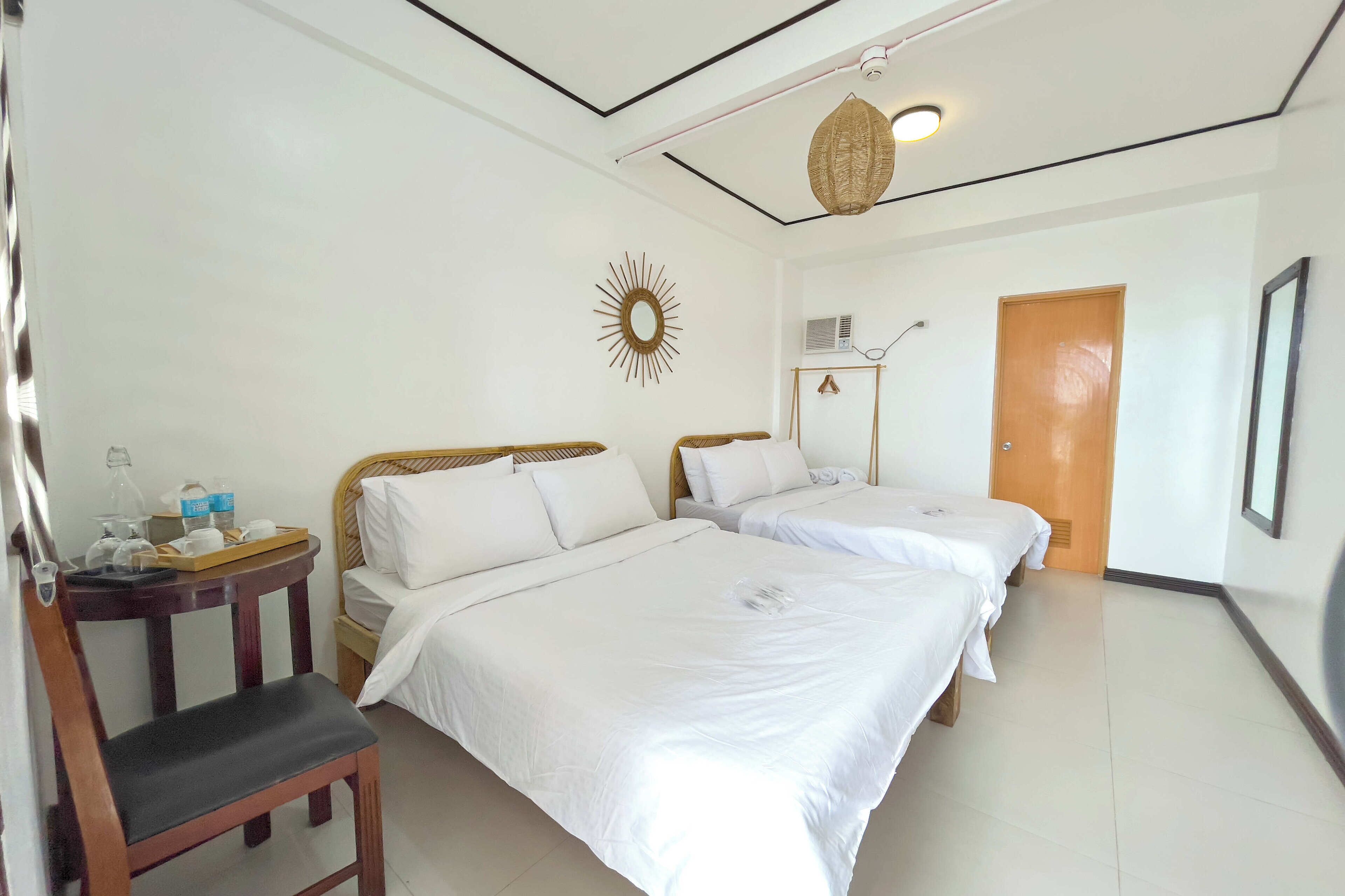 Hotelkamer met twee bedden, een houten stoel, een klein tafeltje met een lamp, een zonvormige decoratie en een deur.