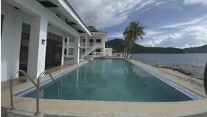 A swimming pool with a view of the sea and mountains. - Salacia Beachfront Resort (Bauan)