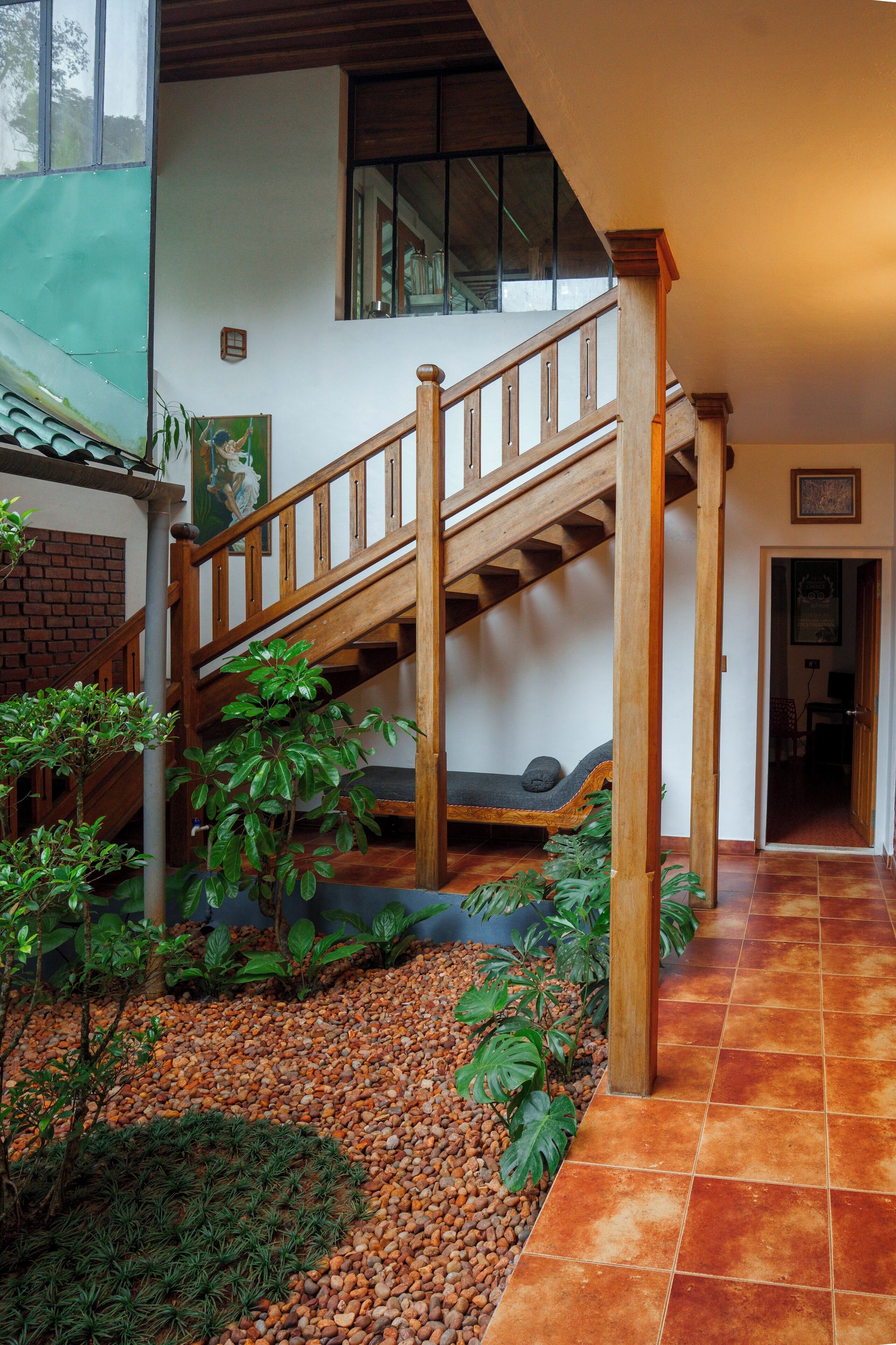 A wooden staircase with a cushioned bench at the bottom, surrounded by indoor plants and pebbles.