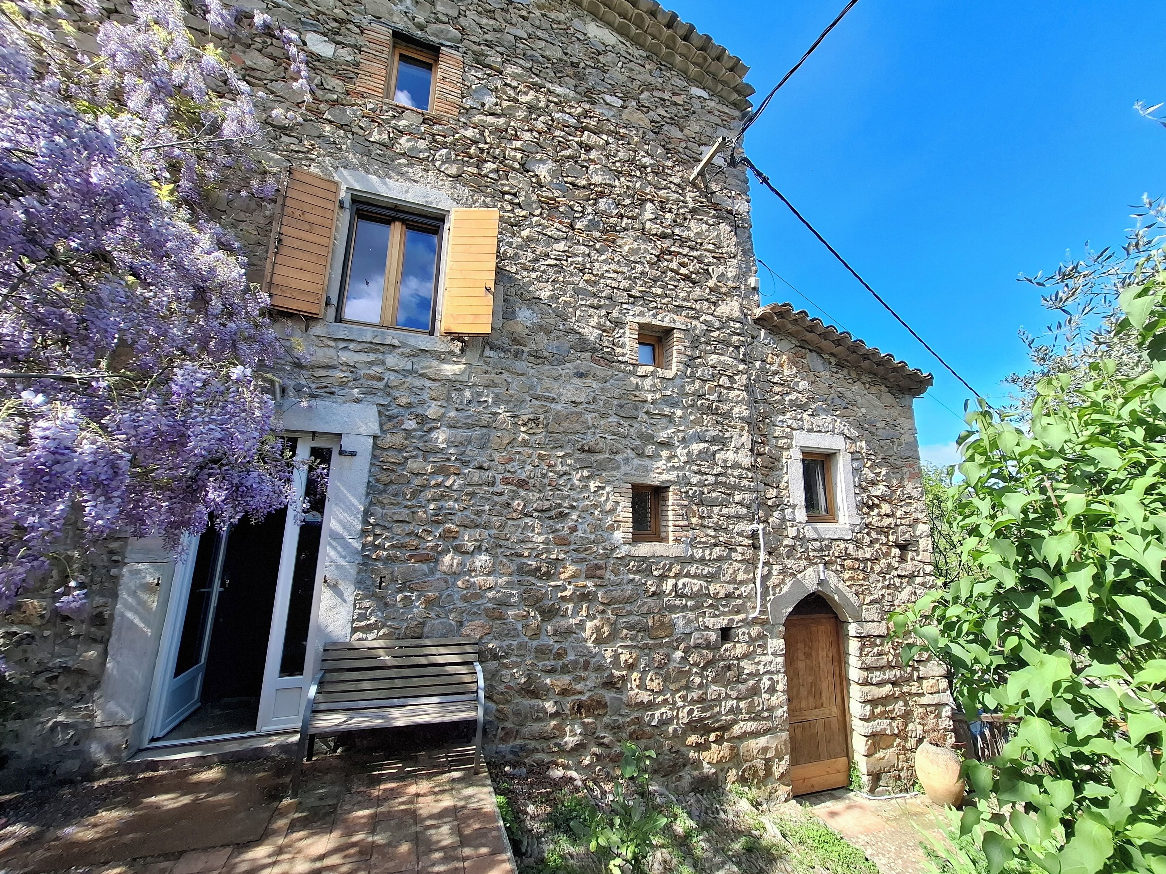 A stone building with a wooden door, a bench outside, and a small garden area.