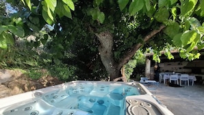 Un jacuzzi con múltiples chorros, rodeado de exuberante follaje y un comedor con mesas y sillas.