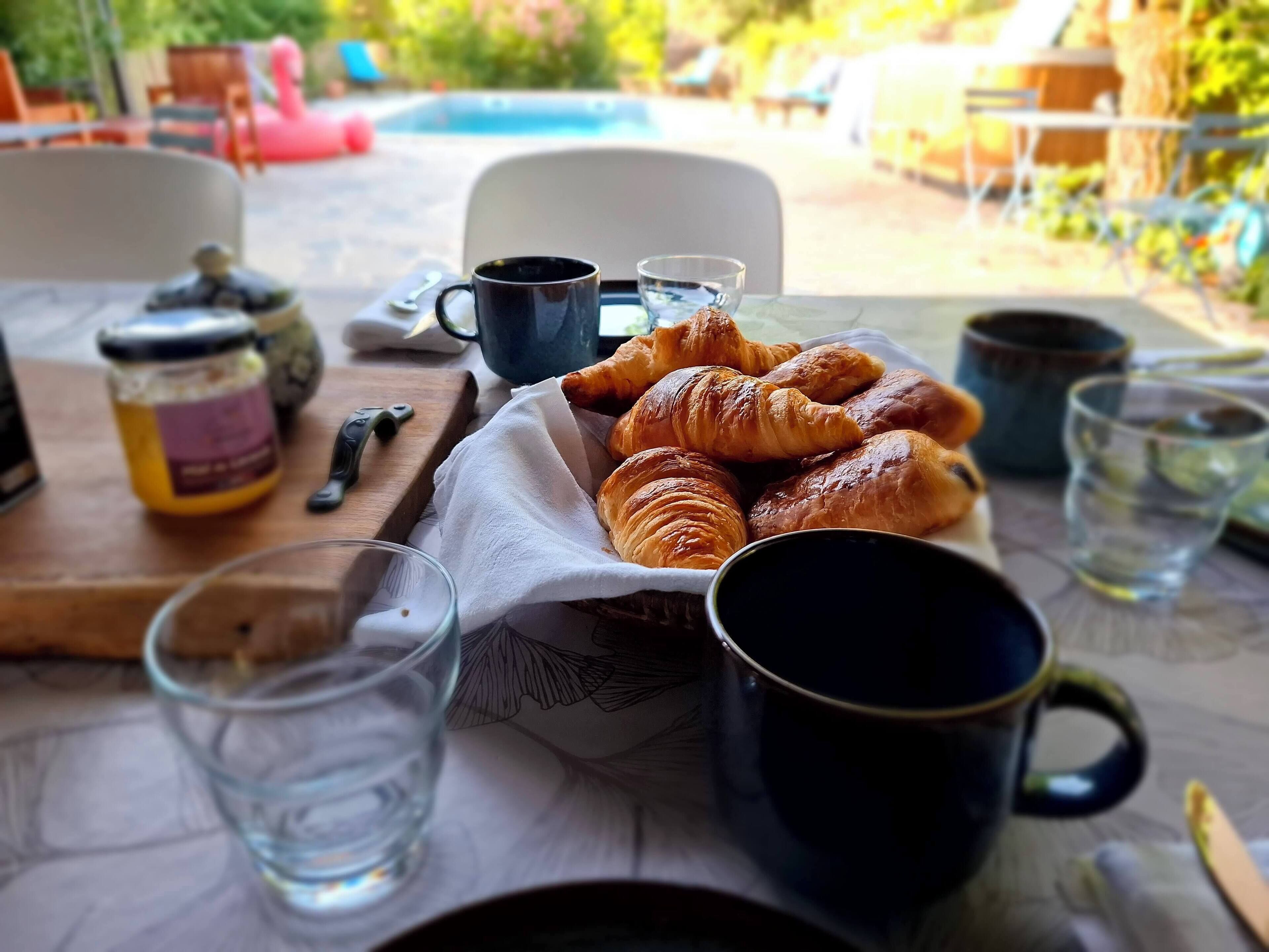 Un desayuno con cruasanes, café y vasos de agua sobre una mesa.