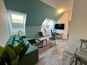 A modern living room with a green sofa, a glass coffee table, and a TV mounted on the wall. - Affordable 3BR Apartment for Groups (Vienna)