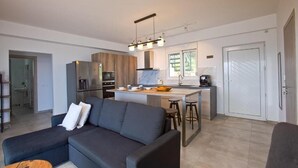 Een moderne keuken met een centraal eiland, een zithoek met een donkerblauwe bank, en een bar voorzien van barkrukken.