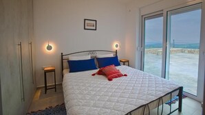 Een slaapkamer met een bed, twee nachtkastjes, een wandlamp en een uitzicht door een groot raam.