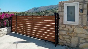 Een omheind toegangspunt met een stenen muur en een metalen poort, op de achtergrond een berglandschap.