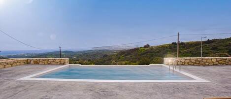 Una piscina rettangolare all'aperto con pareti in pietra, circondata da un solarium in cemento, con vista su un paesaggio collinare.