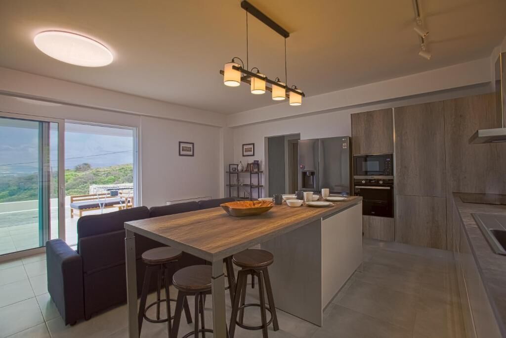 A modern kitchen with a wooden island, bar stools, and a large window offering a view.