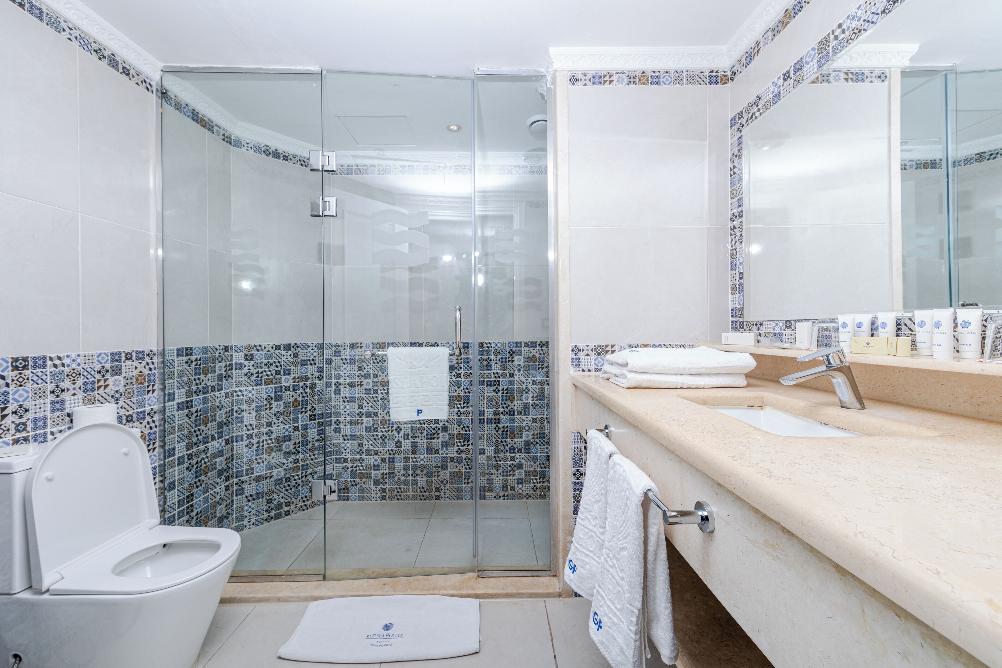 A bathroom with a glass-enclosed shower, a white toilet, a sink with a mirror, and a tiled backsplash.