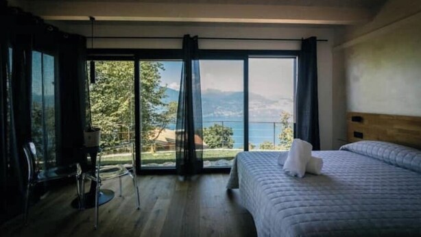 A bedroom with a large window, a bed, and a chair. - Charming bungalow in phenomenal Brenzone sul Garda with AC (Brenzone sul Garda)