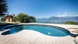 A swimming pool with a wooden deck, surrounded by greenery and a house. - Charming bungalow in phenomenal Brenzone sul Garda with AC (Brenzone sul Garda)