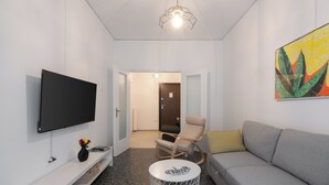 Un soggiorno moderno con una TV a schermo piatto, un divano, una poltrona, un tavolino rotondo e un quadro appeso al muro.
