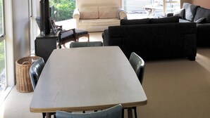 A spacious living area with a large table, sofas, and a fireplace. - Classic 2-bedroom bach in Waihi Beach perfect for relaxing getaway (Waihi Beach)