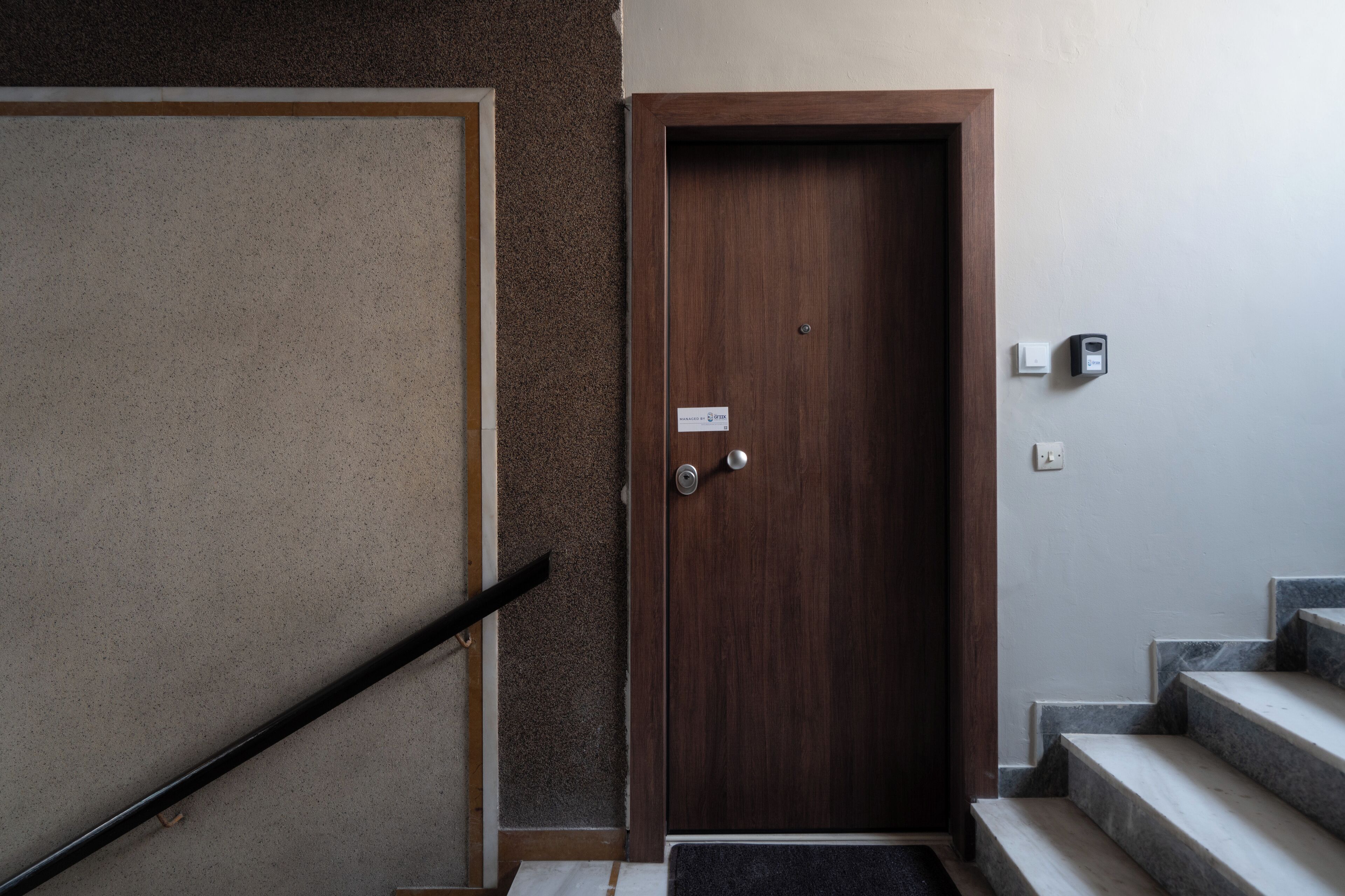 A wooden door with a sign, a handrail, and a set of marble stairs.