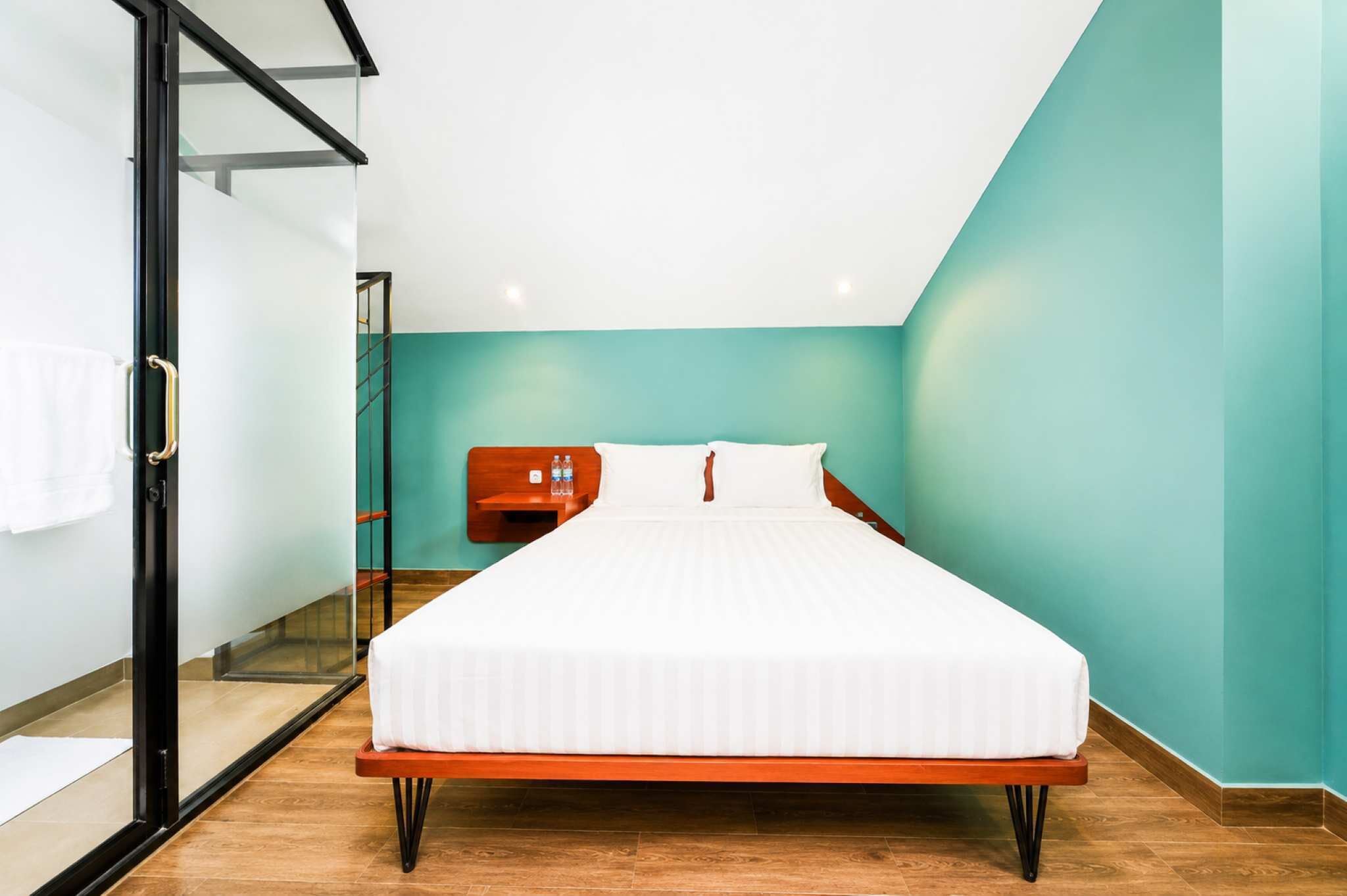 Quarto com cama, mesa de cabeceira, porta de vidro e paredes verde-água.